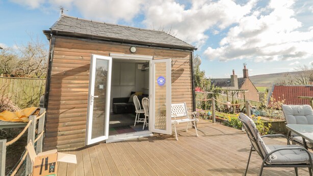 Una cabaña de madera con puerta corredera, un pequeño patio con mobiliario exterior y un jardín.