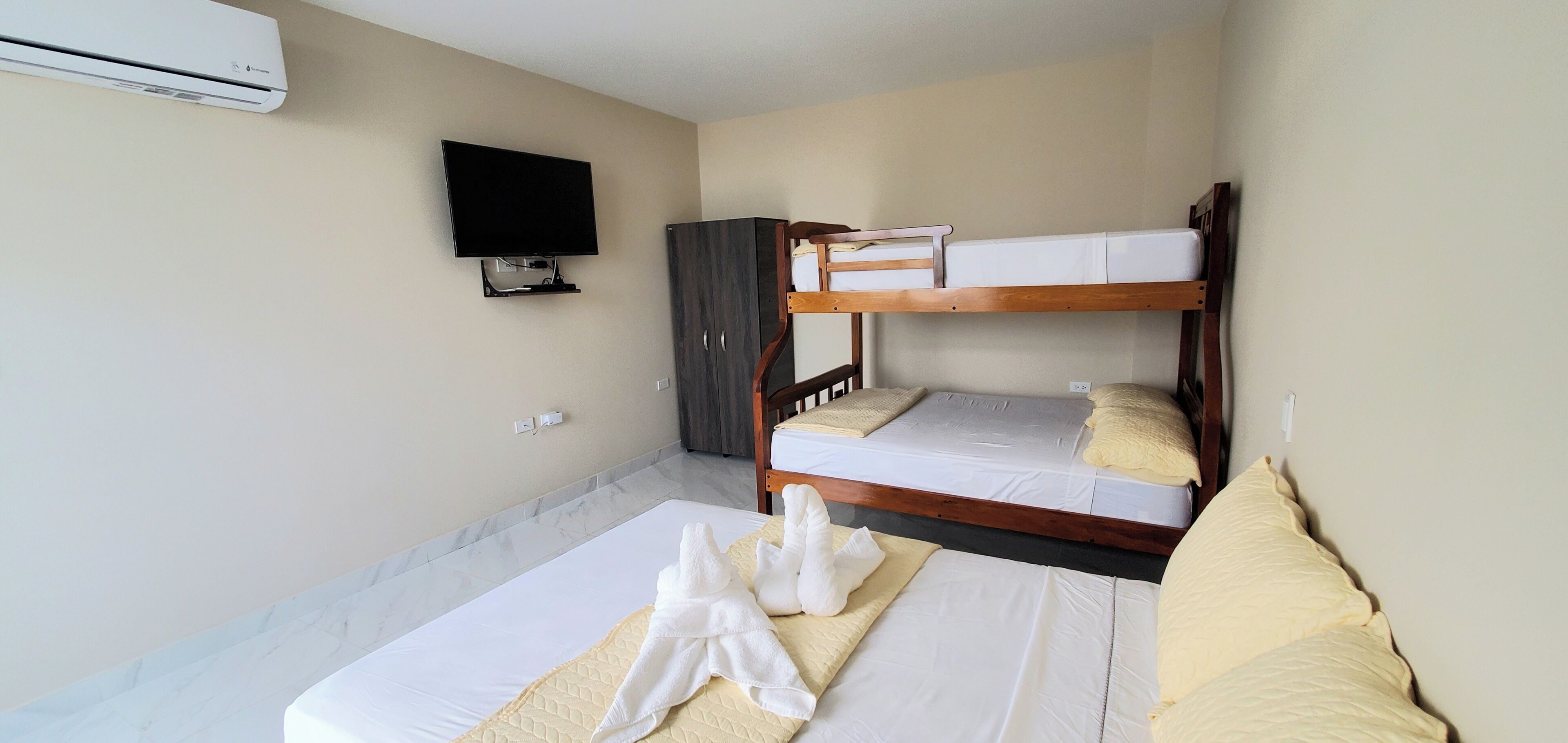 A hotel room with a bunk bed, a television, a wardrobe, and a flat-screen TV mounted on the wall.