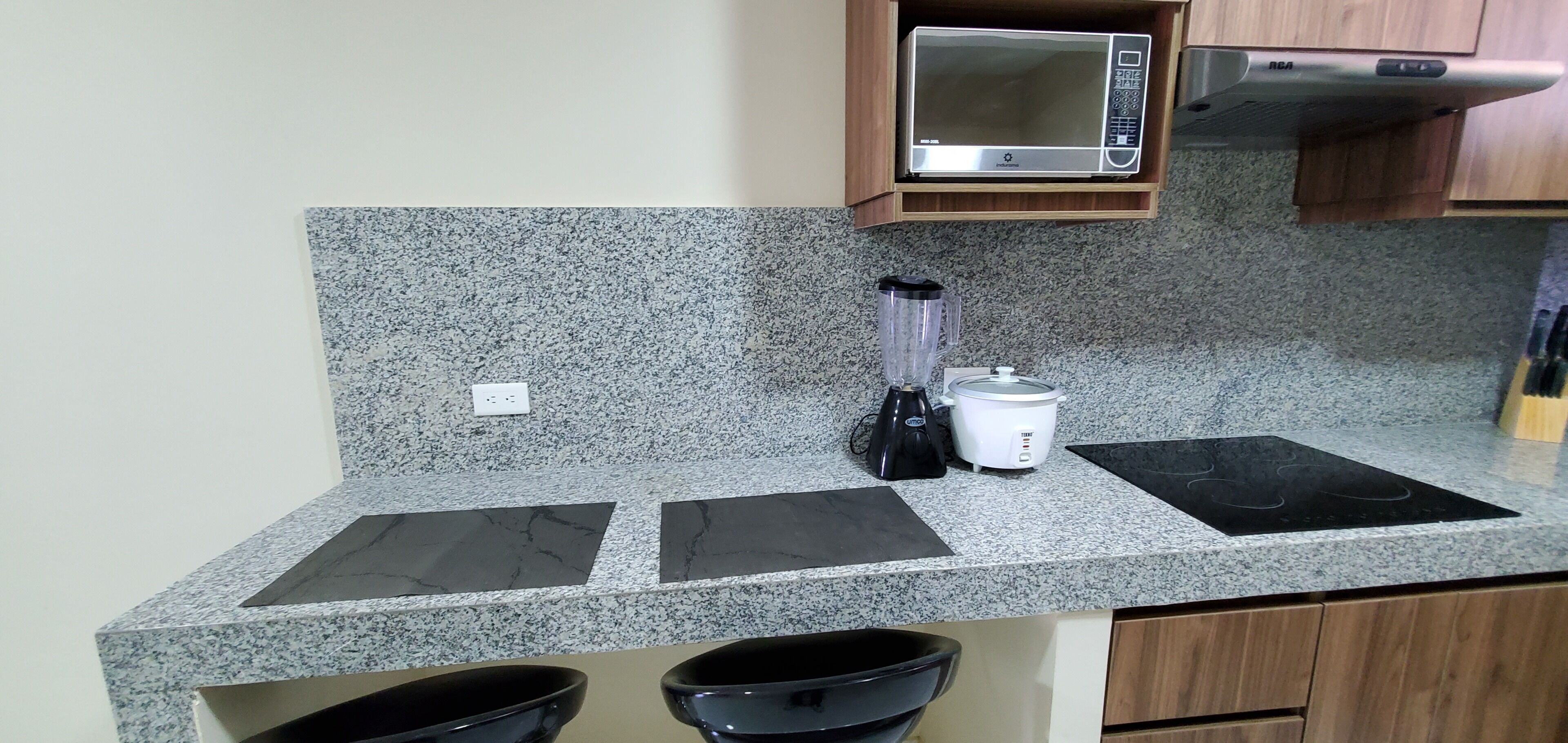 A kitchen with granite countertops, a microwave, a blender, a rice cooker, and a stovetop.