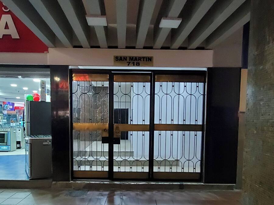 Entrada de un edificio con una verja de metal, un letrero que dice 'SAN MARTIN 718' y un piso de baldosas.
