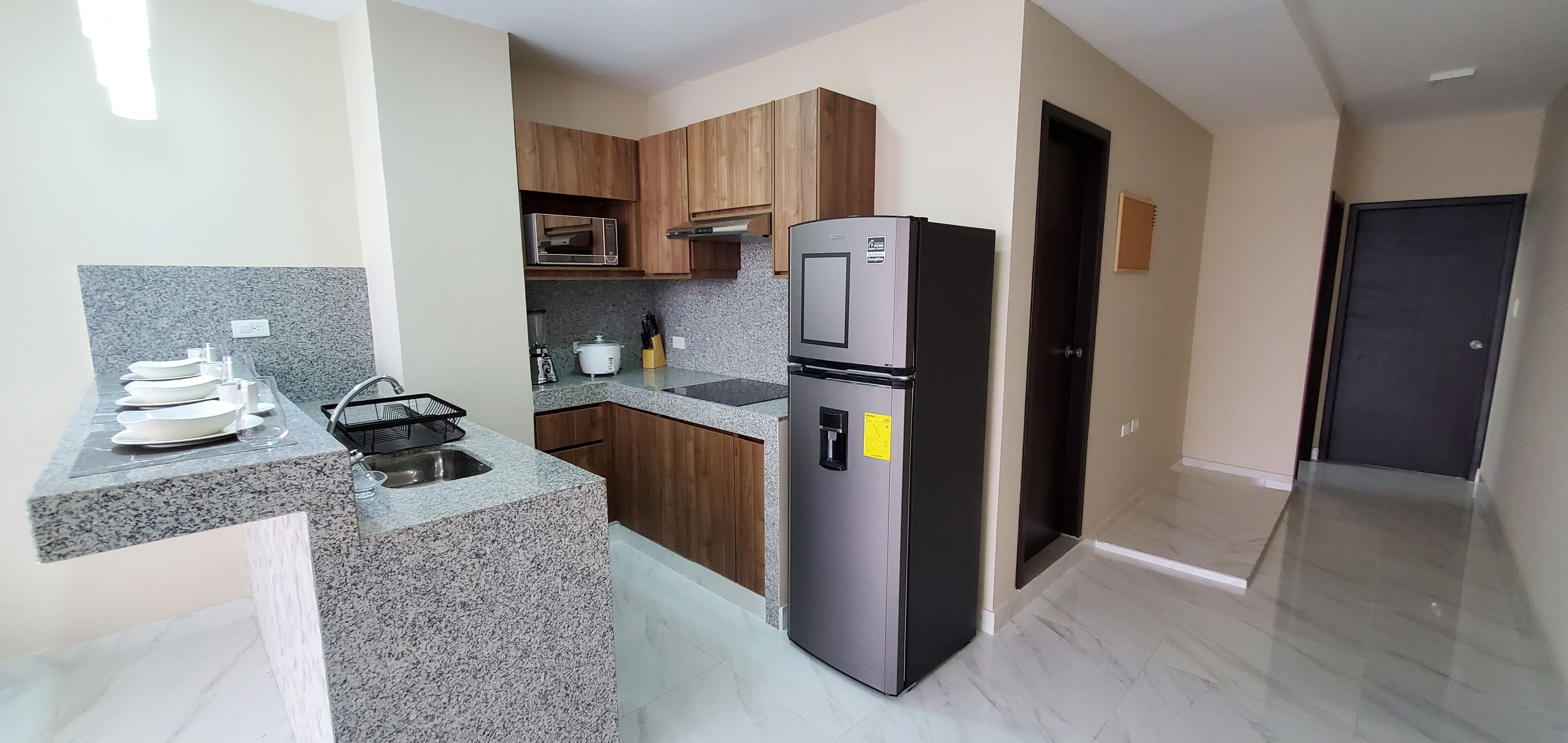 Una cocina con encimeras de granito, refrigerador, armarios de madera y microondas.