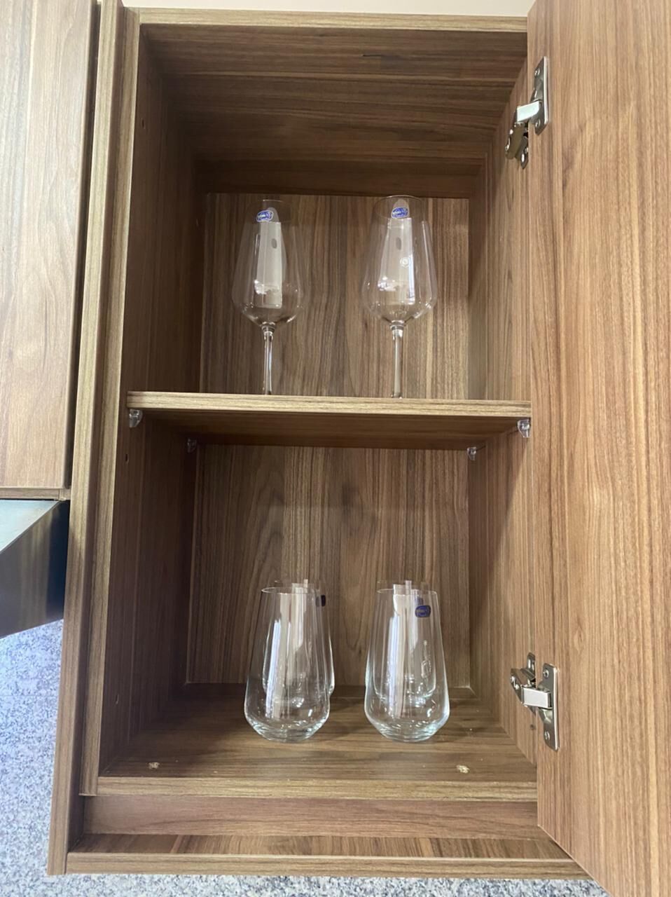 A wooden cabinet with two shelves, each holding a wine glass.