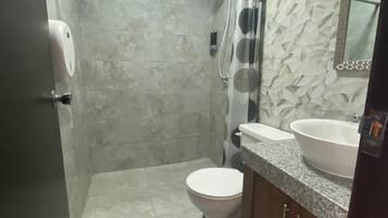 Een badkamer met douche, toilet, wastafel en spiegel.