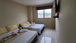 Une chambre d’hôtel avec deux lits, chacun agrémenté d’une serviette en forme de cygne, une fenêtre donnant sur la ville et un téléviseur fixé au mur.