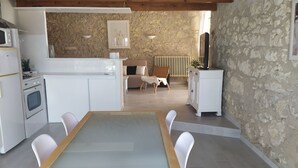 Una cocina moderna con armarios blancos, horno empotrado y comedor con mesa de vidrio y sillas blancas.