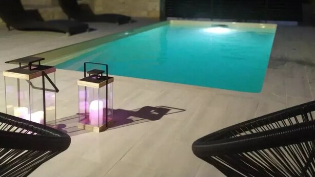 Una piscina al aire libre con sillones de descanso y faroles.