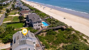 Vista aérea de una propiedad costera con una casa grande, una piscina y una playa.