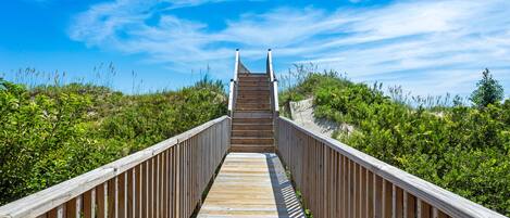 A wooden boardwalk leading to a beach with a clear sky.
