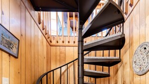 Eine Wendeltreppe mit dunkler Metallreling und Teppichstufen, die zu einer Holzbalkendecke mit Oberlicht führt.