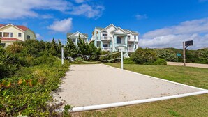 A beachfront property with a sandy volleyball court, a tennis court, and a large house with multiple balconies. - Fun in the Sun: Pool, Hot Tub & Beach (Corolla)