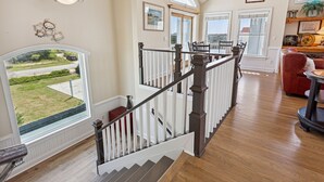 A spacious interior with a wooden staircase, large windows, and a view of the outdoors. - Fun in the Sun: Pool, Hot Tub & Beach (Corolla)