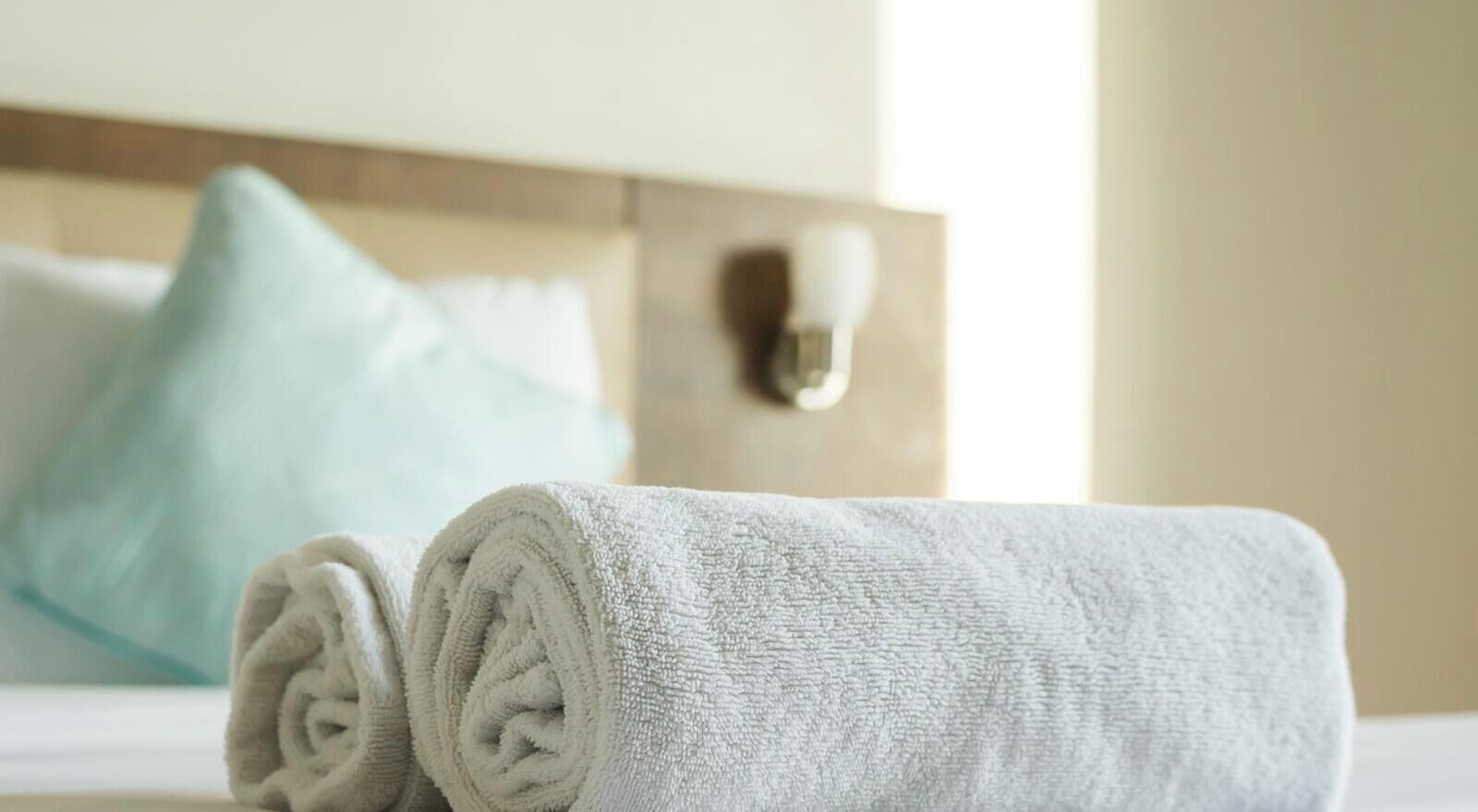 Una toalla blanca doblada con cuidado sobre una cama, con un almohadón al fondo.
