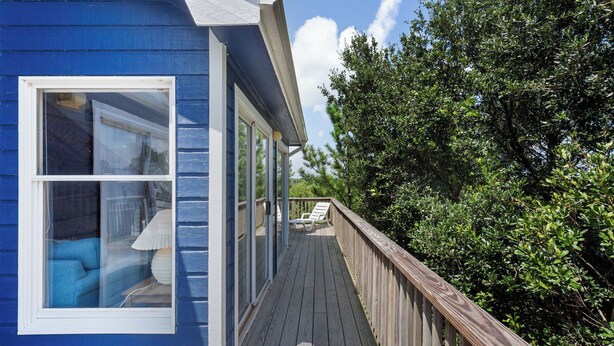 Un edificio azul con una terraza de madera y un área cubierta con una silla blanca.