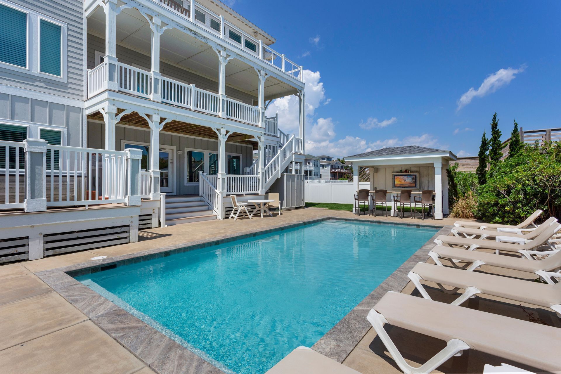 A pool area with a two-story building, outdoor seating, and a covered patio.