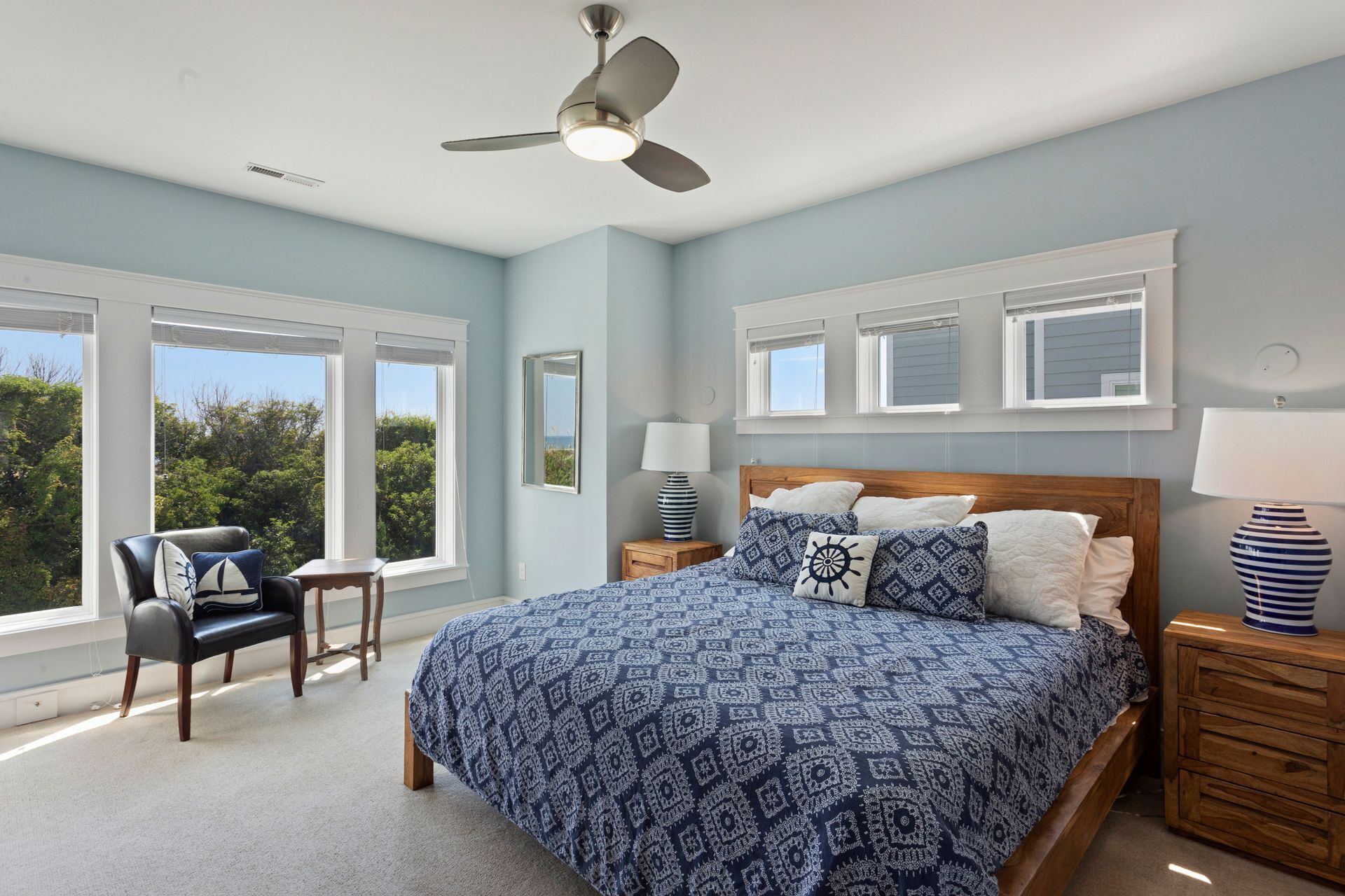 Quarto com uma cama grande, um ventilador de teto, uma cadeira e uma mesa de cabeceira com abajur.