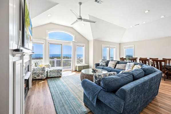 A spacious living room with a large blue sofa, a dining area with wooden chairs, and a view of the ocean through large windows.