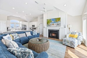 A spacious living room with a fireplace, a large painting, and a view of the kitchen.