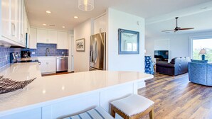 A modern kitchen with a large island, stainless steel appliances, and a dining area with a sofa and a TV. - Ohana Hut: Pool, Hot Tub, 3-Min Walk to Beach (Corolla)