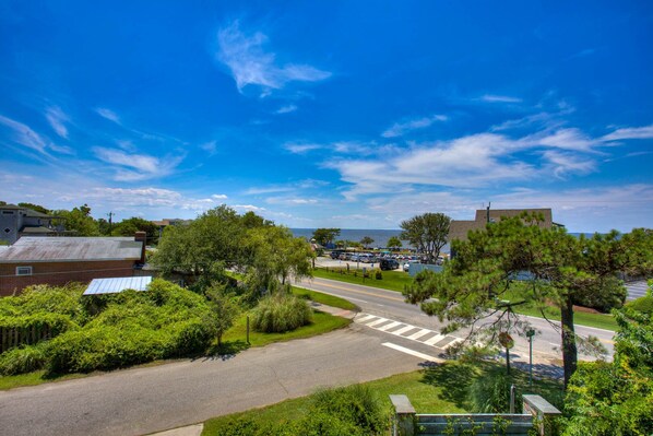 Una calle residencial con casas, cielo azul despejado y vista al mar.