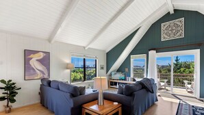 A cozy living room with a high ceiling, a large window, and a view of the outdoors. - Points of View: Panoramic Views, Walk to Beach (Duck)