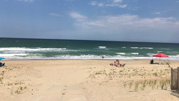 Una playa con arena, algunas personas y un paraguas rojo.