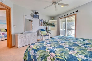 A bedroom with a large bed, a dresser, a chair, a ceiling fan, and a balcony with a view.