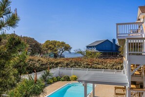 Una piscina con muelle blanco, una casa azul al fondo y un cielo despejado.