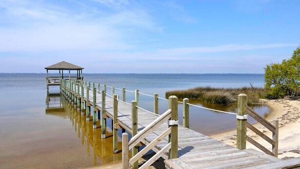 A wooden pier extending into calm waters, a covered shelter at the end, and a sandy beach with sparse vegetation. - Merryweather: Pool, Hot Tub, Ocean + Sound Access (Duck)