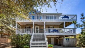 A two-story building with a staircase leading to the entrance, surrounded by trees and potted plants. - Merryweather: Pool, Hot Tub, Ocean + Sound Access (Duck)