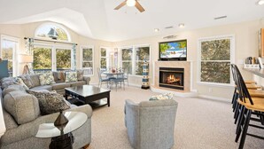 A spacious living room with a fireplace, a ceiling fan, and a television mounted above it. - Merryweather: Pool, Hot Tub, Ocean + Sound Access (Duck)