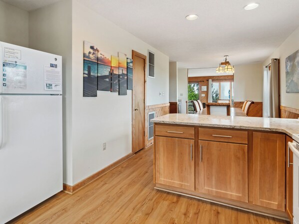 A modern kitchen with wooden cabinets, a marble countertop, and a view to the dining area. - Horizon's Summit: Ocean Views, 2-Min Walk Beach (Duck)