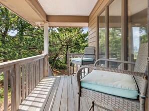 A wooden deck with a wicker chair and a cushion, overlooking a forested area. - Horizon's Summit: Ocean Views, 2-Min Walk Beach (Duck)