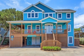 A two-story house with a blue exterior, a front porch with wooden railings, and a small front yard. - Sol Mates: Pool, Tiki Bar, 3-Min Walk Beach OBX (Duck)