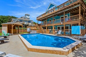 A two-story wooden building with a swimming pool, outdoor seating, and a covered area.
