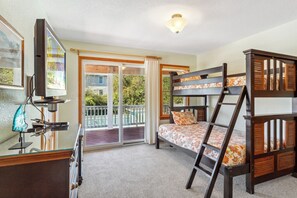A room with bunk beds, a television, a desk with a computer, and a balcony with a view of greenery. - Taste of Paradise: Pool, Hot Tub, Elevator, OBX (Duck)