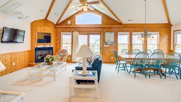 A spacious living area with a high ceiling, wooden walls, a fireplace, a television, and a dining set. - Morning View: Ocean Views, Pool, Hot Tub, Game Room (Southern Shores)