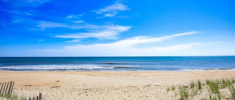 Una playa con arena, una valla de madera y escasa hierba.