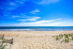 A beach with sand, a wooden fence, and sparse grass.