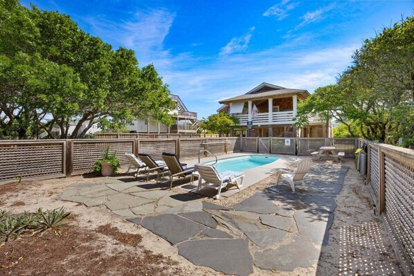 A backyard with a swimming pool, lounge chairs, and a wooden deck.