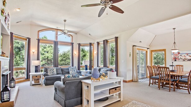 Un espacio habitable espacioso con chimenea, ventanas amplias y una zona de comedor con mobiliario de madera.