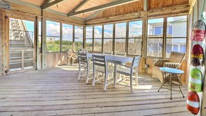 A covered outdoor area with a wooden deck, a table with chairs, and large windows offering views of the surrounding landscape.