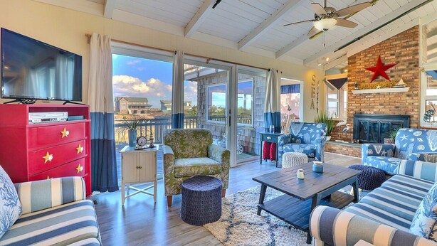A spacious living room with a large TV, comfortable seating, a fireplace, and a view of the sea.