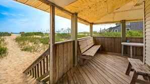 Um deck de madeira com um banco e mesa, com vista para uma praia arenosa e oceano.