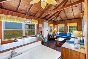 A rustic cabin interior with a kitchen area, a dining table, and a seating area with a sofa and chairs.