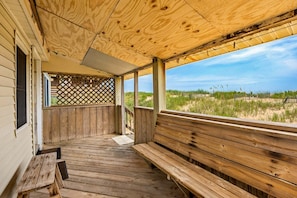 Eine Holzterrasse mit Bänken, einem Gitter und Blick auf den Strand.