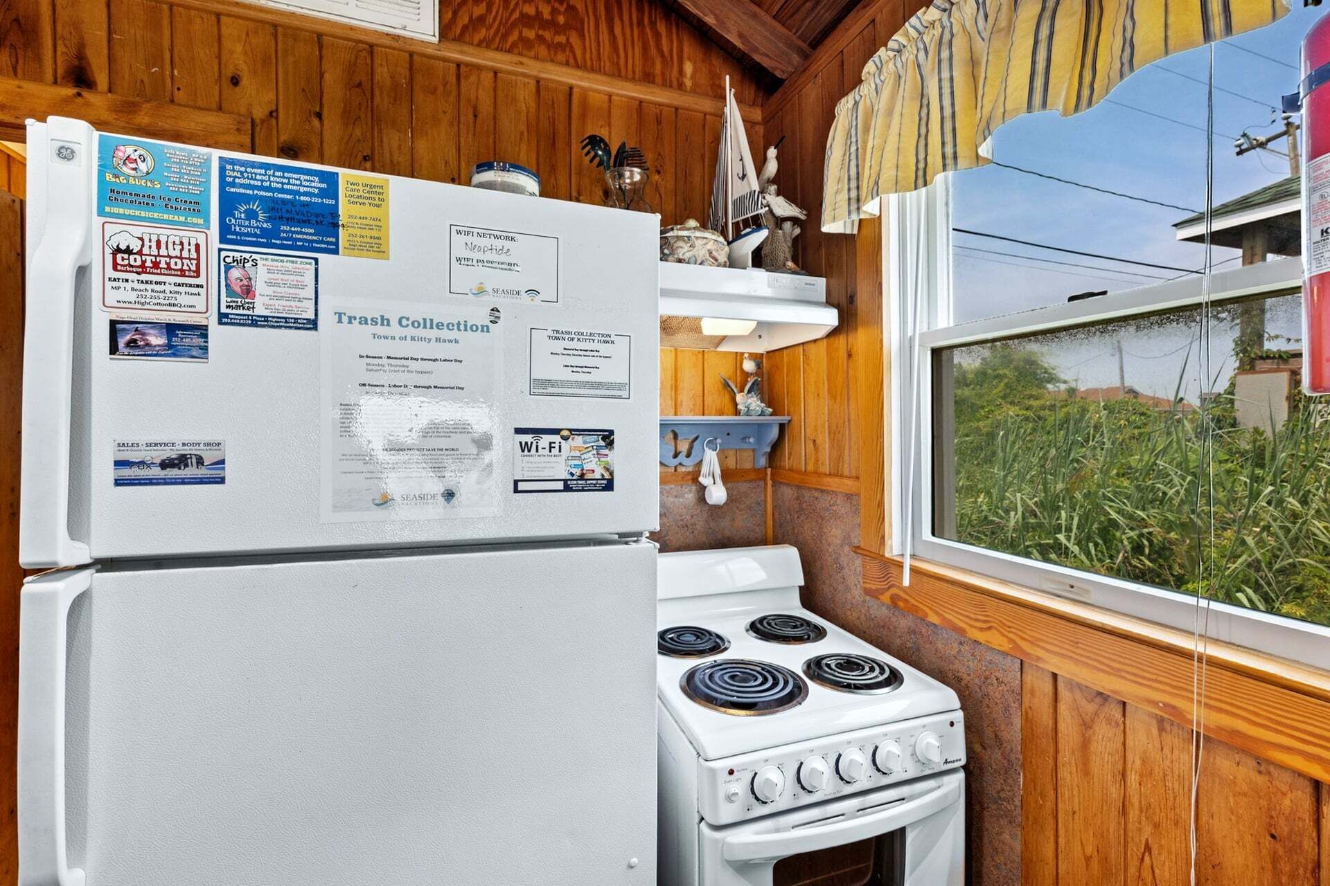 A kitchen with a white refrigerator, stove, and a window with a view of greenery.