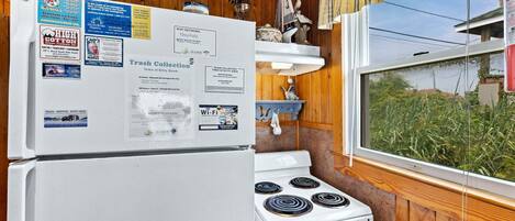 A kitchen with a white refrigerator, stove, and a window with a view of greenery.