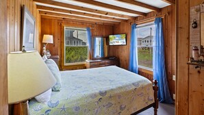 Quarto com cama, televisão, janela com cortinas e teto de madeira.