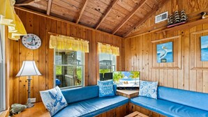 Interior de cabana com teto de madeira, um relógio, televisão e um sofá azul com almofadas decorativas.