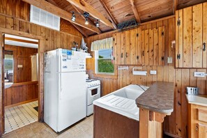 A compact kitchen with wooden walls, a white refrigerator, a stove, and a sink.
